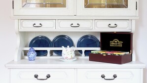 A white cabinet with glass doors, three blue plates, a teapot, and a box of tea. - stylish, idyllic apartment with mountain view (Stegen)