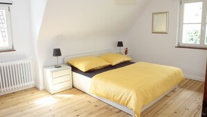 A bedroom with a bed, nightstands, a lamp, a radiator, and a window. - stylish, idyllic apartment with mountain view (Stegen)