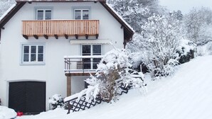 A two-story house with a wooden balcony, a garage, and snow-covered surroundings. - stylish, idyllic apartment with mountain view (Stegen)