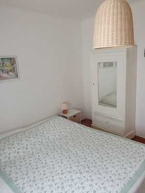 Un dormitorio con una cama, una mesita de noche con lámpara, un armario y un espejo.