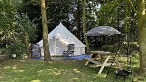 A tent with a picnic table and chairs in a wooded area. - Spacious Bell Tent at Herigerbi Park, Lincolnshire (Grantham)