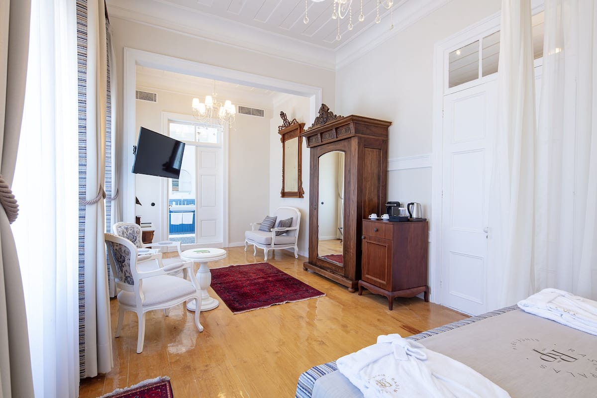 Hotellihuone, jossa on puulattia, suuri peili, vaatekaappi, taulutelevisio, pieni pyöreä pöytä tuoleineen ja punainen matto.