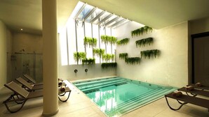 An indoor swimming pool with glass walls, lounge chairs, and hanging plants. - Rasim Palas (Adults Only +12) (Cesme)