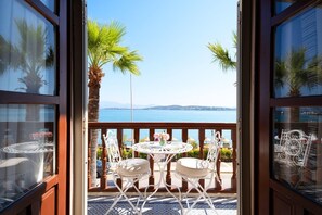 An open balcony with a table and chairs, overlooking a body of water and distant land.