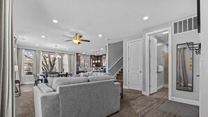 Una sala de estar moderna con un sofá gris, un comedor, una cocina y una escalera que sube a otro nivel.