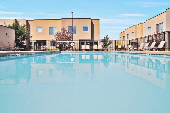 A swimming pool with lounge chairs and a building with multiple windows and doors.