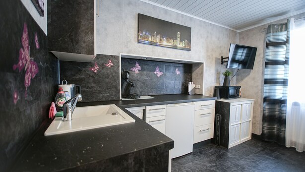 Una cocina moderna con encimera negra, armarios blancos, un lavabo y un televisor de pantalla plana montado en la pared.