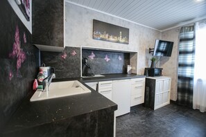 A modern kitchen with a black countertop, white cabinets, a sink, and a flat-screen TV mounted on the wall.