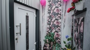 Una puerta con el número '2' en la parte superior, una puerta blanca de marco negro, y una pared con papel tapiz floral y faroles rosados colgando.