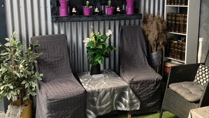 Un rincón acogedor con dos sillones, una mesita con un florero y una estantería frente a una pared de metal corrugado.