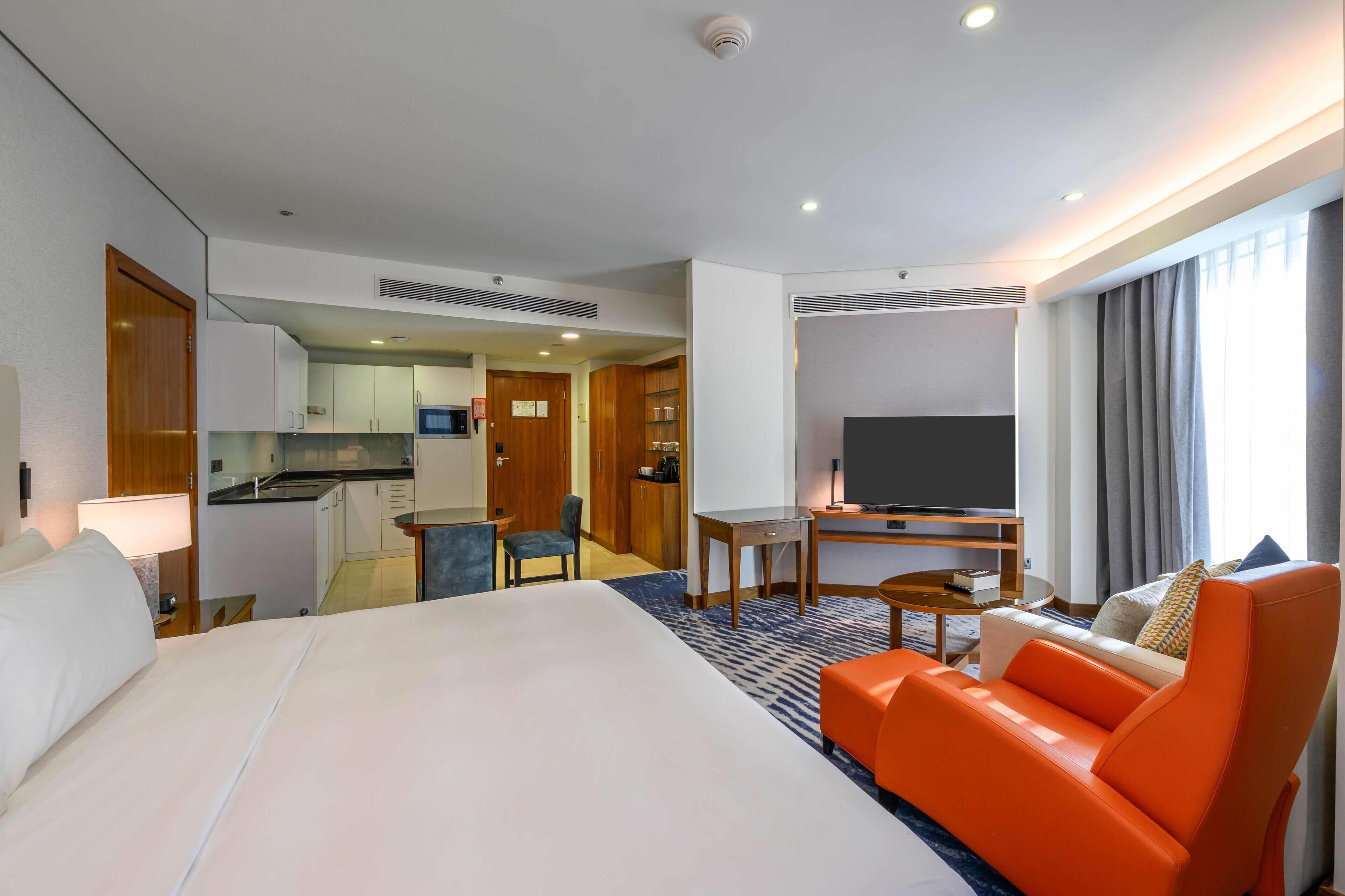 A hotel room with a bed, a sofa, a TV, a desk, and a kitchenette.