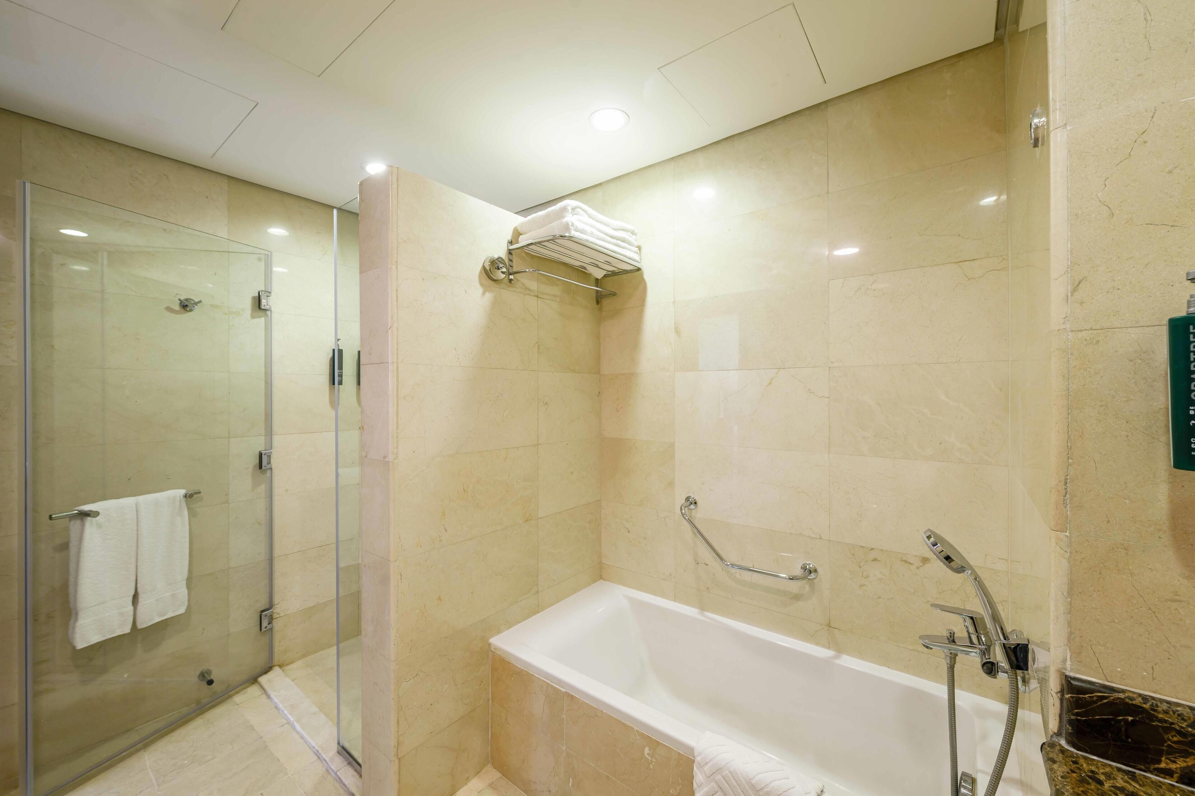 A modern bathroom with a glass-enclosed shower, a bathtub with a handheld showerhead, and a towel rack with folded towels.