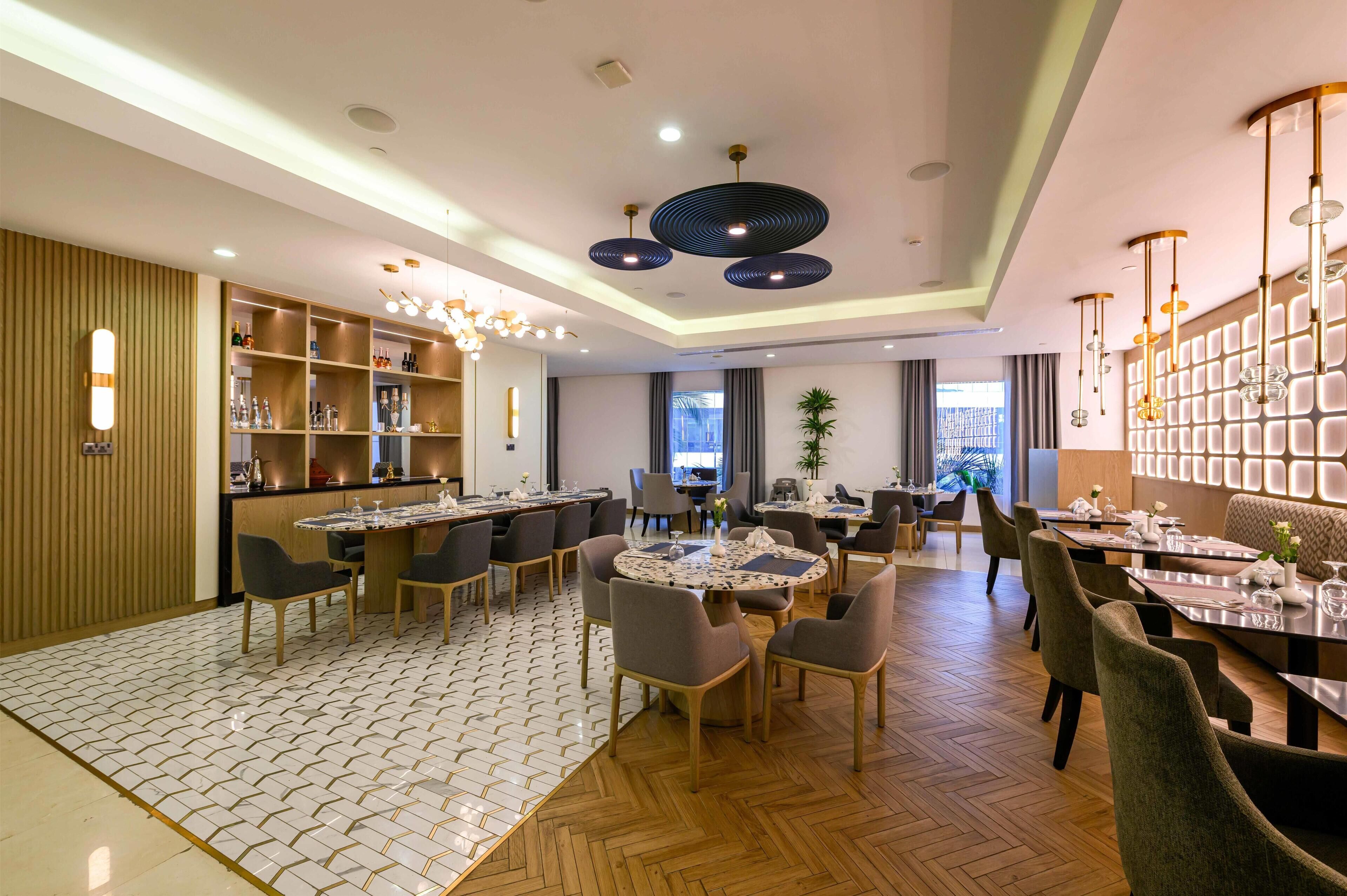 A modern dining area with round tables, chairs, and a bar area with shelves.