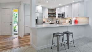 Una cocina moderna con armarios blancos, un refrigerador de acero inoxidable, un microondas y una isla grande con dos taburetes.