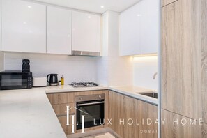 A modern kitchen with white cabinets, a gas stove, a microwave, and a coffee maker. - LUX Contemporary Suite Marina View 3 (Dubai)