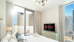 A luxury hotel room with a large bed, a flat-screen TV, and a view of tall buildings. - LUX Contemporary Suite Marina View 3 (Dubai)