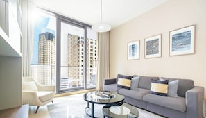 A modern living room with a grey sofa, a round coffee table, and a large window offering a city view. - LUX Contemporary Suite Marina View 3 (Dubai)