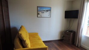 Ett vardagsrum med en gul soffa, en platt-TV som är monterad på väggen och ett träskåp.