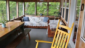 A cozy cabin interior with a wooden dining table, benches, a sofa with patterned cushions, and a chair with a decorative headrest. - "Andy's Place" (Abbot)