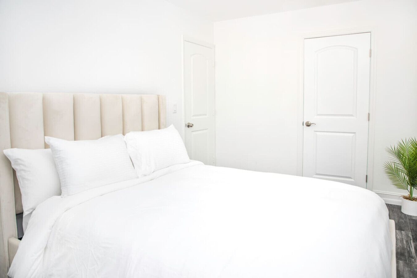 A white bed with a headboard, white walls, and two white doors.