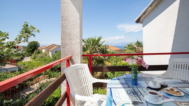 Un balcon avec une table dressée pour deux personnes, une chaise blanche et une rambarde rouge.