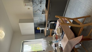 Un coin repas avec une table dressée pour quatre personnes, des chaises en bois et, en arrière-plan, une vue sur une cuisine et une salle de bain.