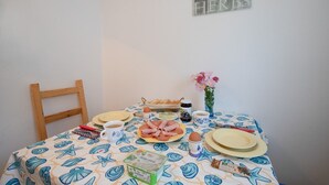 Une table à manger recouverte d’une nappe à motifs de fruits de mer, avec des assiettes, du pain, des œufs et un pot de confiture.