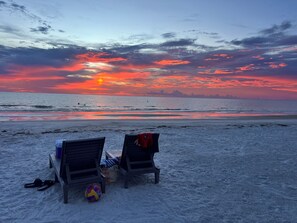 Two beach chairs facing the ocean with a sunset view.