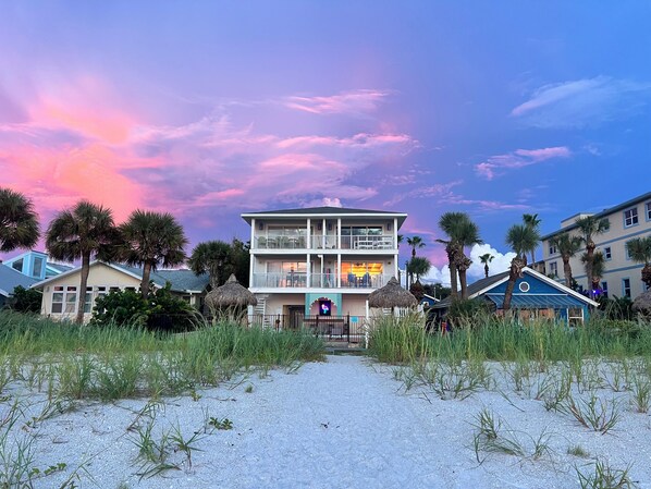 A beachfront hotel with a two-story structure, a visible entrance, and a thatched-roof building in the foreground.