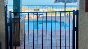 A pool area with a thatched umbrella, a chair, and a fence.