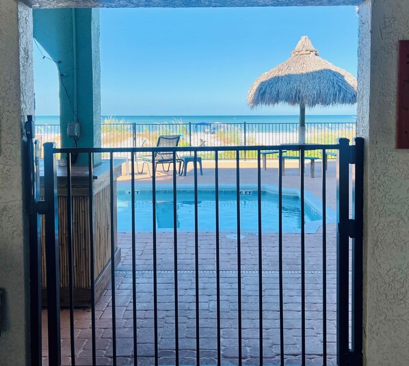 A pool area with a thatched umbrella, a chair, and a fence.