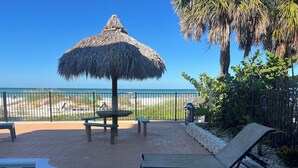 A poolside area with a thatched umbrella, lounge chairs, and a view of the beach.