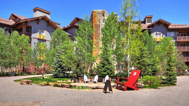 A building with a stone tower, surrounded by trees and outdoor seating areas. - Modern Hotel Room in Center Village - TM225A by Redawning (Copper Mountain)
