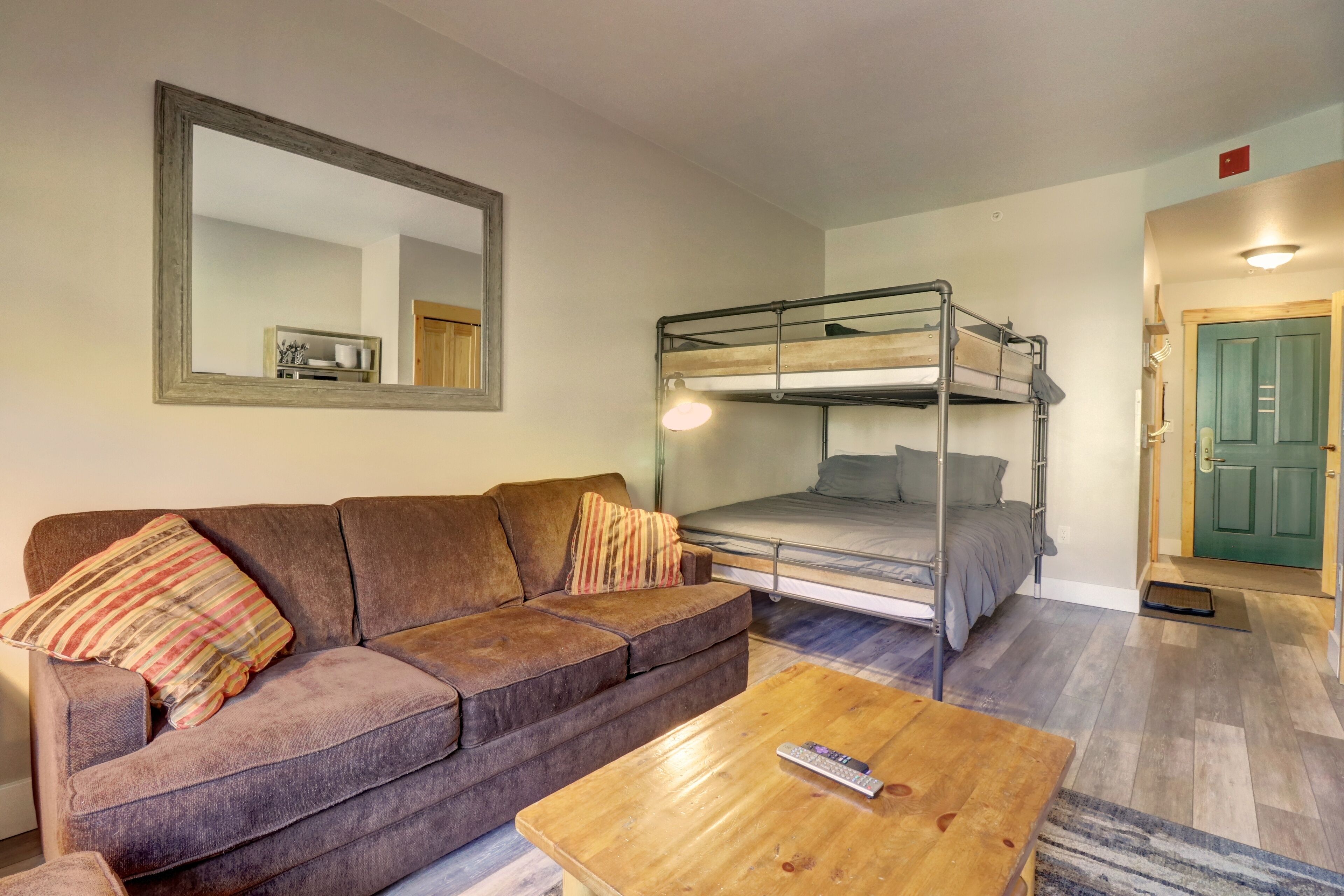 A room with a bunk bed, a sofa, a coffee table, and a mirror.