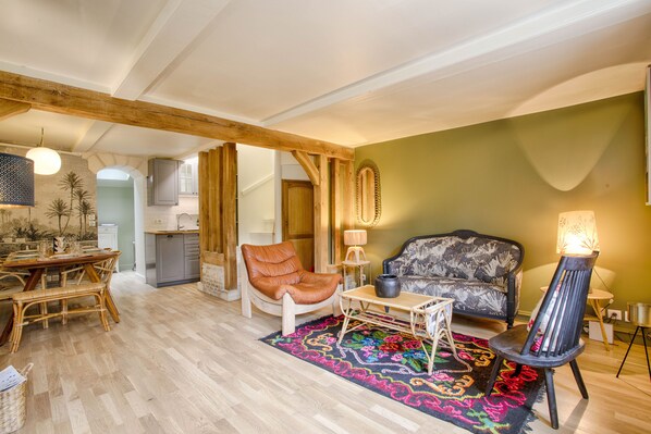 A spacious living area with a wooden ceiling, a dining table with chairs, a sofa, and a patterned rug.