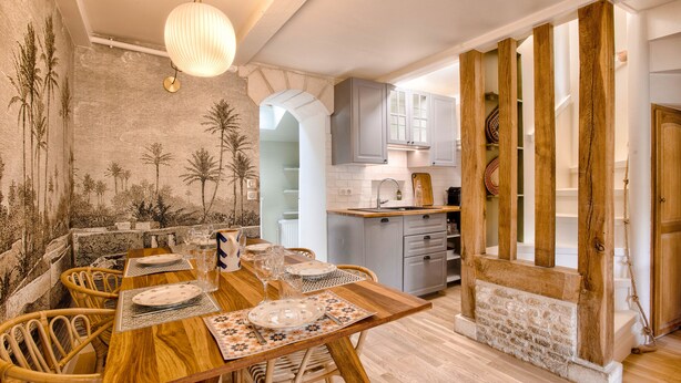 A dining area with a wooden table set for four, surrounded by wicker chairs. A kitchen with grey cabinets and a white countertop is visible in the background. - Villa Bougainvillier - quays of Trouville-sur-Mer (Trouville-sur-Mer)