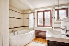 A modern bathroom with a freestanding bathtub, a large sink, and a window with blinds.