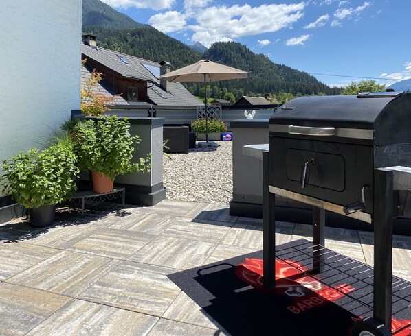 A patio with a barbecue grill, potted plants, and a view of mountains.