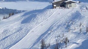 Une montagne enneigée, avec un bâtiment d’une station de ski et un télésiège en arrière-plan.