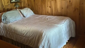 Une chambre à coucher dans une cabane en bois, avec un lit, une table de chevet et un tableau encadré au mur.