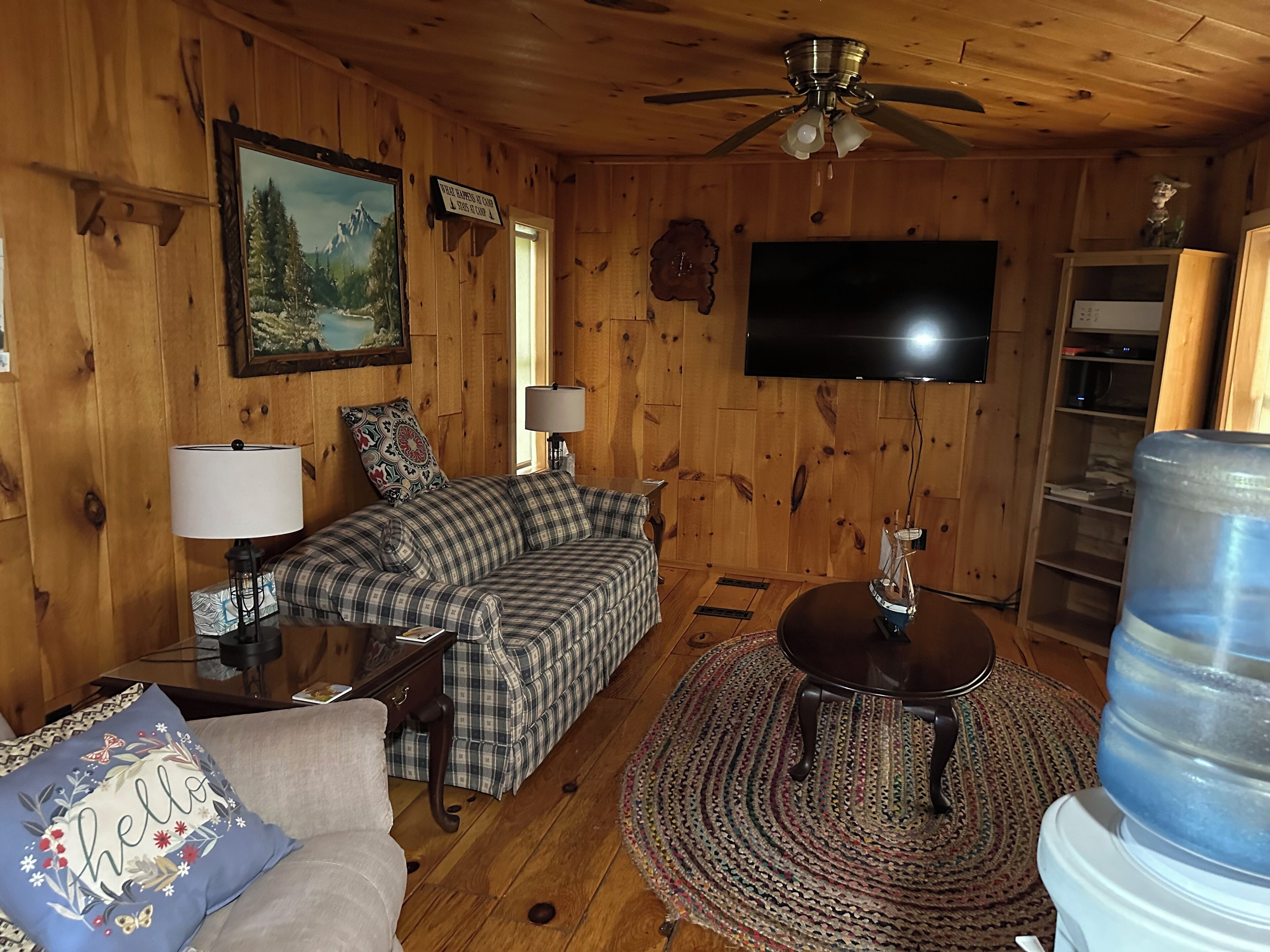 A cozy wooden interior with a sofa, a coffee table, a television, and a water dispenser.