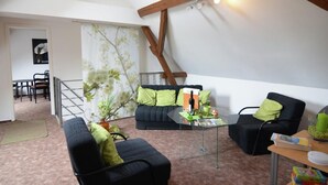 Uma sala de estar acolhedora com um sofá, poltronas e uma mesa de centro. Uma escada leva a um andar superior.