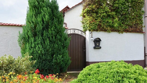 Uma casa com portão fechado, caixa de correio e diversos canteiros com plantas e flores no jardim.