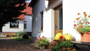 Uma casa com telhado de telhas vermelhas, um caminho de tijolos e vasos com flores laranjas.
