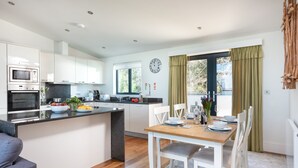 A modern kitchen with built-in appliances, a dining area with a wooden table and white chairs, and a large window with curtains.