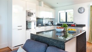A modern kitchen with white cabinetry, a central island with a bowl of fruit, and a clock on the wall.