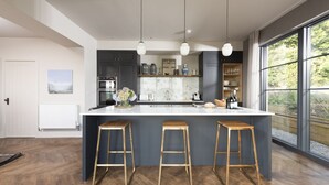 Una cucina moderna con una grande isola, tre sgabelli, mobili scuri e vista sul verde attraverso ampie finestre.