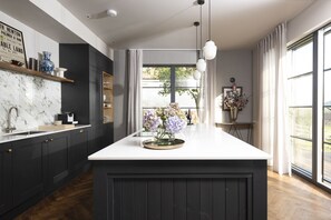 A modern kitchen with dark cabinetry, a marble countertop, and pendant lighting.