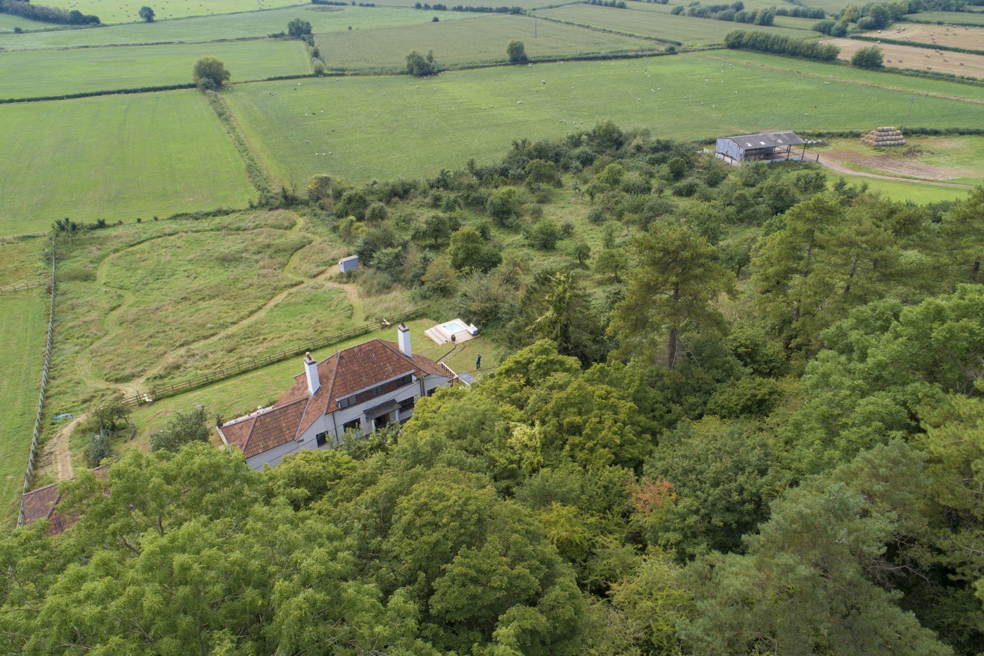 En landejendom med et stort hus omgivet af marker og træer.