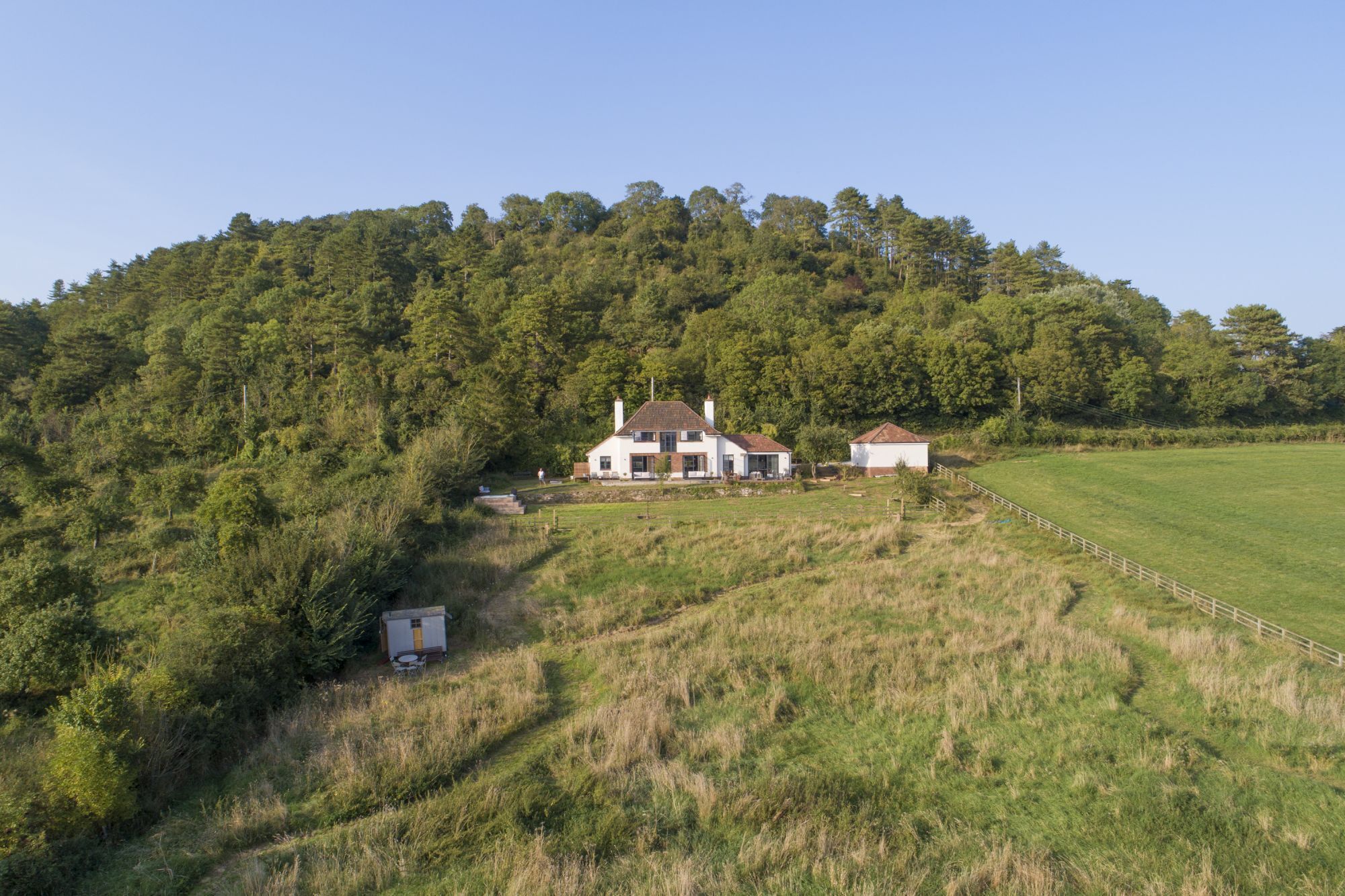 A large house with a spacious lawn and a forested hill in the background.
